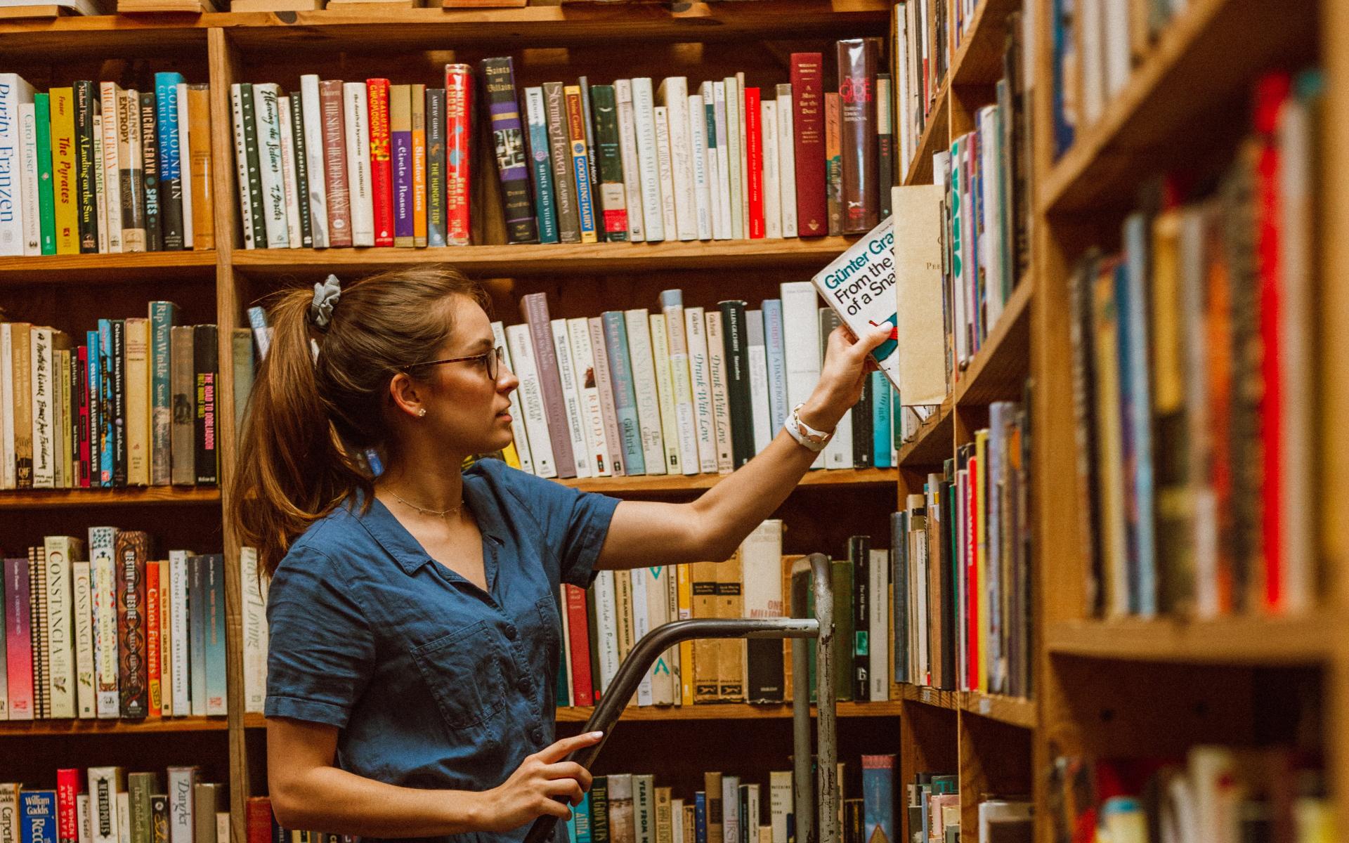 Junge Frau auf einer Leiter vor dem Bücherregal